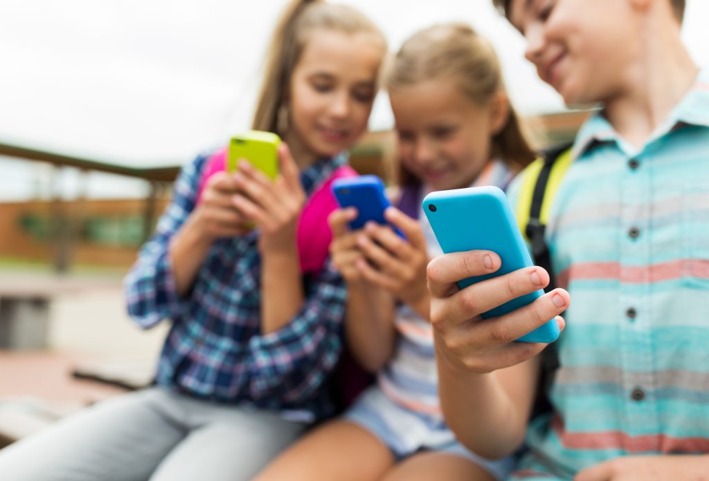 Drei Kinder sitzen nebeneinander und schauen jeweils auf ein Smartphone.
