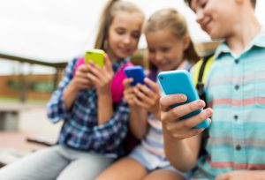 Drei Kinder sitzen nebeneinander und schauen jeweils auf ein Smartphone.